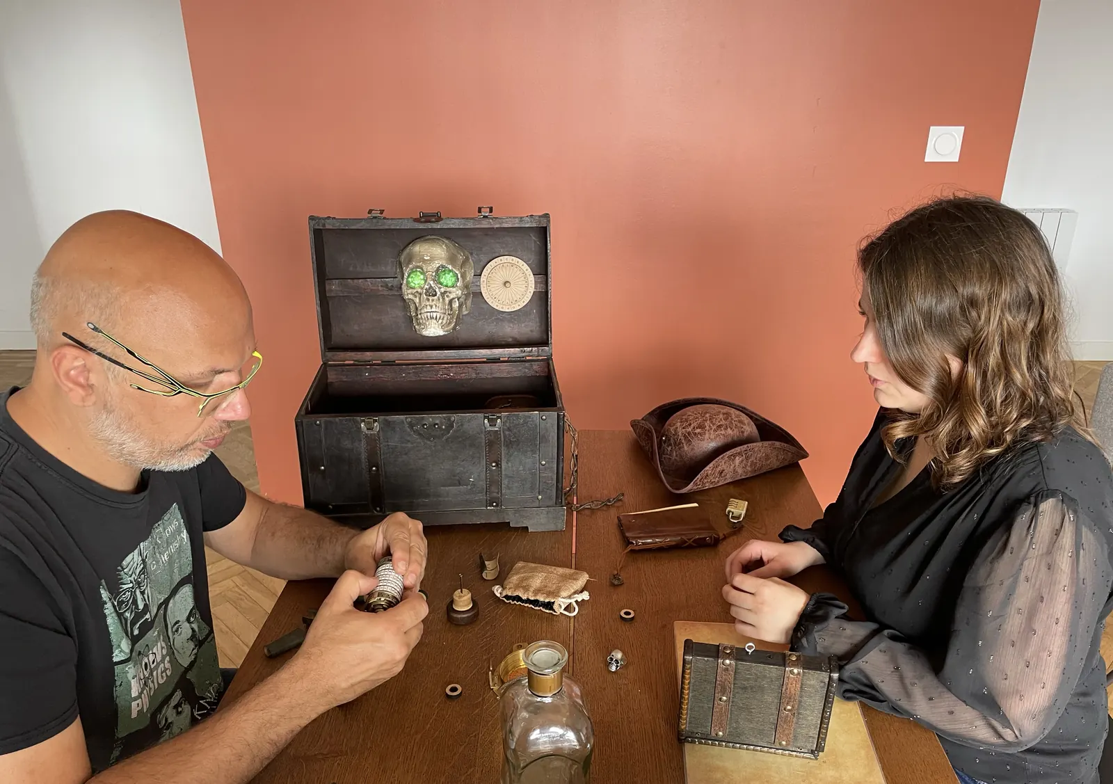 Deux joueurs face au coffre Pirate ouvert, sur une table en bois chargée d'objets